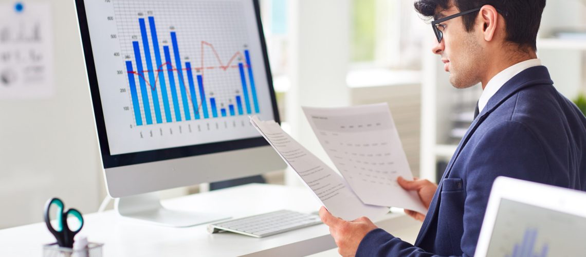 Businessman looking through papers by workplace and analyzing statistics